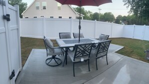 A patio with a table and chairs, a red umbrella, and a white fence in the background. - 3-bedroom bungalow in charming Easley with AC, WiFi (Easley)