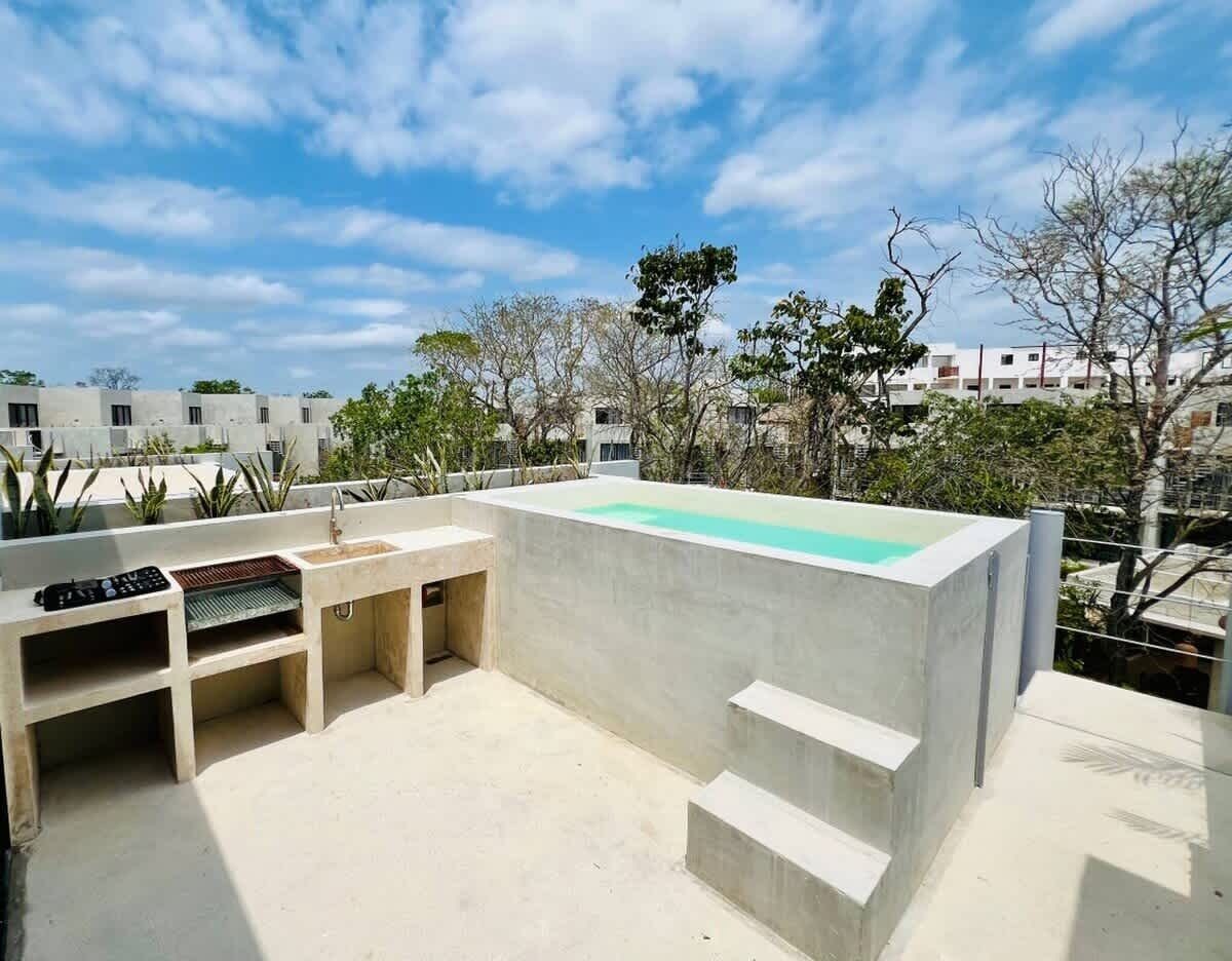 Un patio al aire libre con piscina de concreto, parrilla integrada y escaleras que conducen a una terraza.