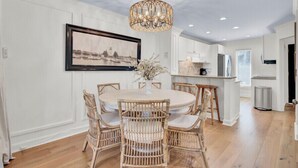 A dining area with a round table, wicker chairs, a chandelier, and a framed cityscape picture on the wall.