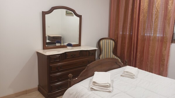 Una camera da letto con una cassettiera in legno, un letto con biancheria bianca, una sedia e uno specchio.