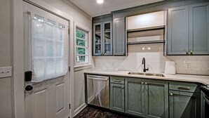 A kitchen with white cabinets, a stainless steel dishwasher, a sink, and a window with a view of greenery. - Peaceful Clinton Retreat in Olde Towne (Clinton)