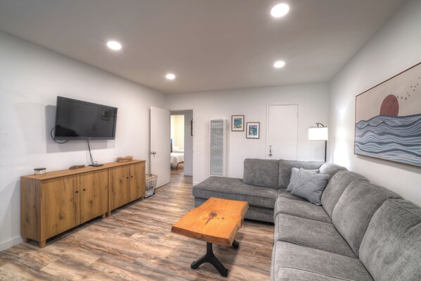A modern living room with a grey sofa, wooden cabinet, and a TV mounted on the wall. - Beautiful 2 bed w/Ocean view - private wifi (Carpinteria)