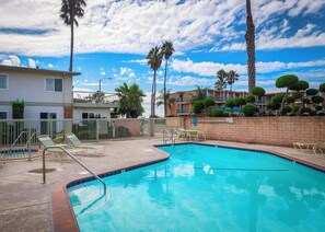 A swimming pool with lounge chairs and palm trees, surrounded by buildings. - Beautiful 2 bed w/Ocean view - private wifi (Carpinteria)