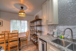 A kitchen with a granite countertop, stainless steel sink, wooden chairs, a dining table, and a ceiling light fixture.