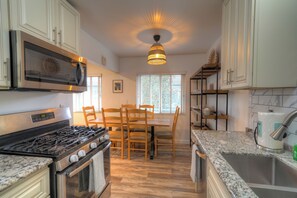 A kitchen with a gas stove, oven, microwave, granite countertop, and a dining area with wooden chairs and a table.