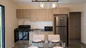 A modern kitchen with wooden cabinets, a stainless steel refrigerator, a microwave, and a gas stove. There is a dining table set with plates, glasses, and cutlery.