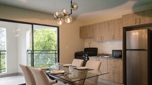 A modern kitchen with a glass dining table, wooden cabinets, and a stainless steel refrigerator.