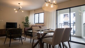 A modern living room with a dining area, large windows, and a flat-screen TV.