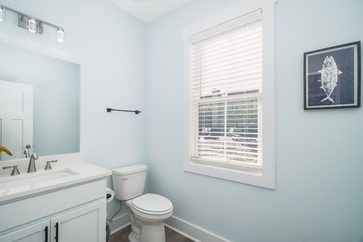 A bathroom with a white sink, toilet, and window with blinds.