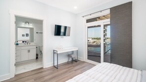 Ein modernes Schlafzimmer mit einem großen Bett, einem Schreibtisch und einem Fernseher. Ein Balkon bietet Blick auf die Stadt.