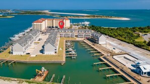 Luftaufnahme einer Marina mit mehreren Anlegestellen, einem großen Gebäudekomplex und freiem Blick auf das umliegende Wasser und Land.