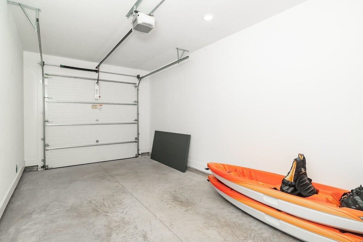 A garage with a closed garage door, a ceiling-mounted projector, and an orange kayak with gear on the floor.