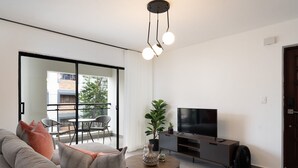 A modern living room with a sofa, a coffee table, a TV, and a balcony with a view of a building and trees. - Modern 2BR ·Gazcue · 5min to Monuments · YellowKey (Santo Domingo)