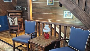 Une pièce chaleureuse avec un bureau en bois, deux chaises bleues, une petite table avec une lampe et un tapis décoratif.