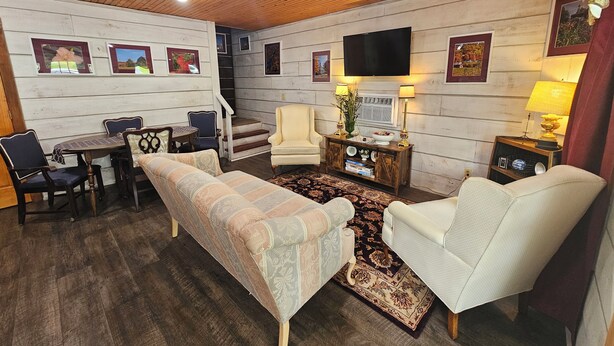 Un salon confortable avec un canapé, des fauteuils, une table basse et un téléviseur. Un escalier mène à un autre niveau.