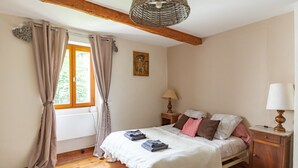 Une chambre avec un plancher en bois, un lit recouvert d’une courtepointe blanche, deux lampes de chevet, une table de chevet en bois et une fenêtre avec des rideaux.