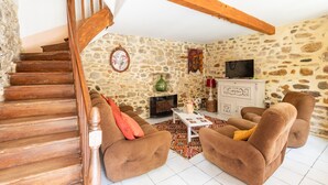 Un salon chaleureux avec un mur en pierre, un escalier en bois et une cheminée.