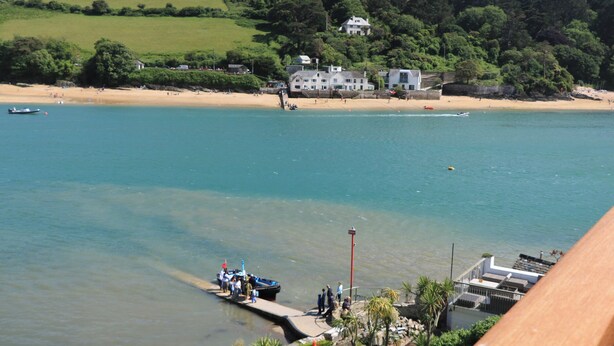 Une vue sur la côte, avec un quai, une grande maison située sur une colline et une plage de sable.