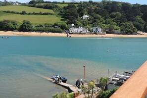 A coastal view with a dock, a large house on a hill, and a sandy beach. - 43 The Salcombe (Salcombe)