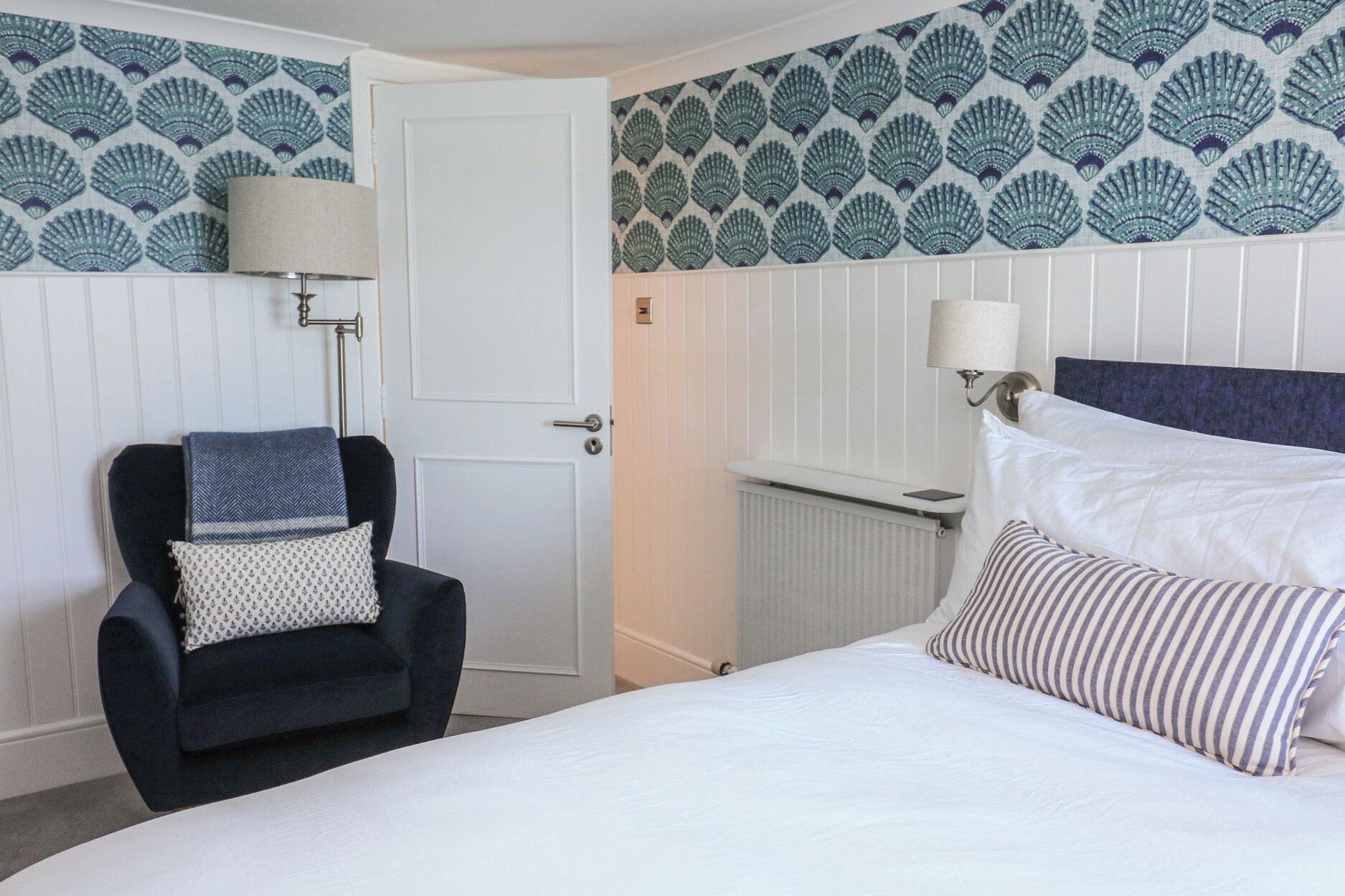 Una habitación de hotel con una cama, una silla, una puerta y una pared con diseño de conchas.
