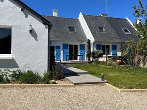 Une maison moderne à deux étages, avec une allée en gravier, un petit jardin et une porte bleue.