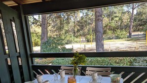 Un espacio de estar al aire libre cubierto con una mesa y sillas, con vista a un área boscosa.
