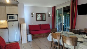 Un espacio habitable compacto con kitchenette, un sofá, una mesa de comedor con sillas y un televisor montado en la pared.