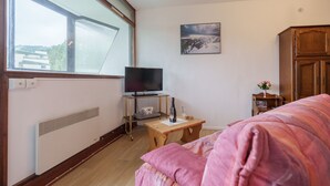 Une pièce confortable avec un lit, un téléviseur posé sur un meuble, un radiateur et une fenêtre donnant sur un paysage enneigé.