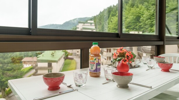 Une table à manger avec différents bols et une bouteille de jus, placée devant une fenêtre donnant sur un paysage verdoyant.