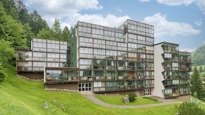 Un bâtiment moderne à plusieurs étages, doté de grandes fenêtres en verre et d’une façade verdoyante, entouré d’une pelouse et d’arbres.