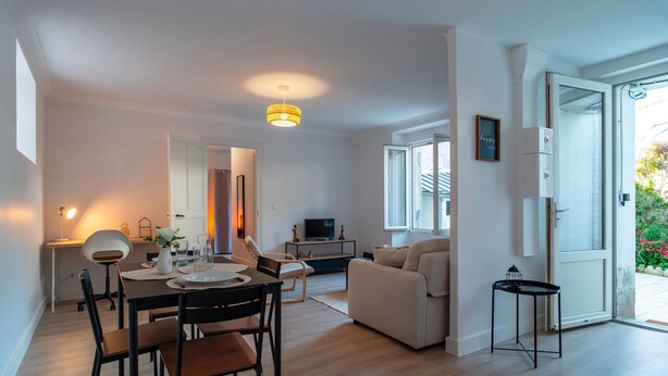 Una sala de estar moderna con comedor, un sofá, un televisor y una mesita de noche con lámpara.