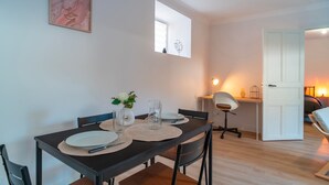 Un comedor con una mesa dispuesta para dos personas, una silla, un pequeño jarrón con flores y una obra de arte enmarcada en la pared.