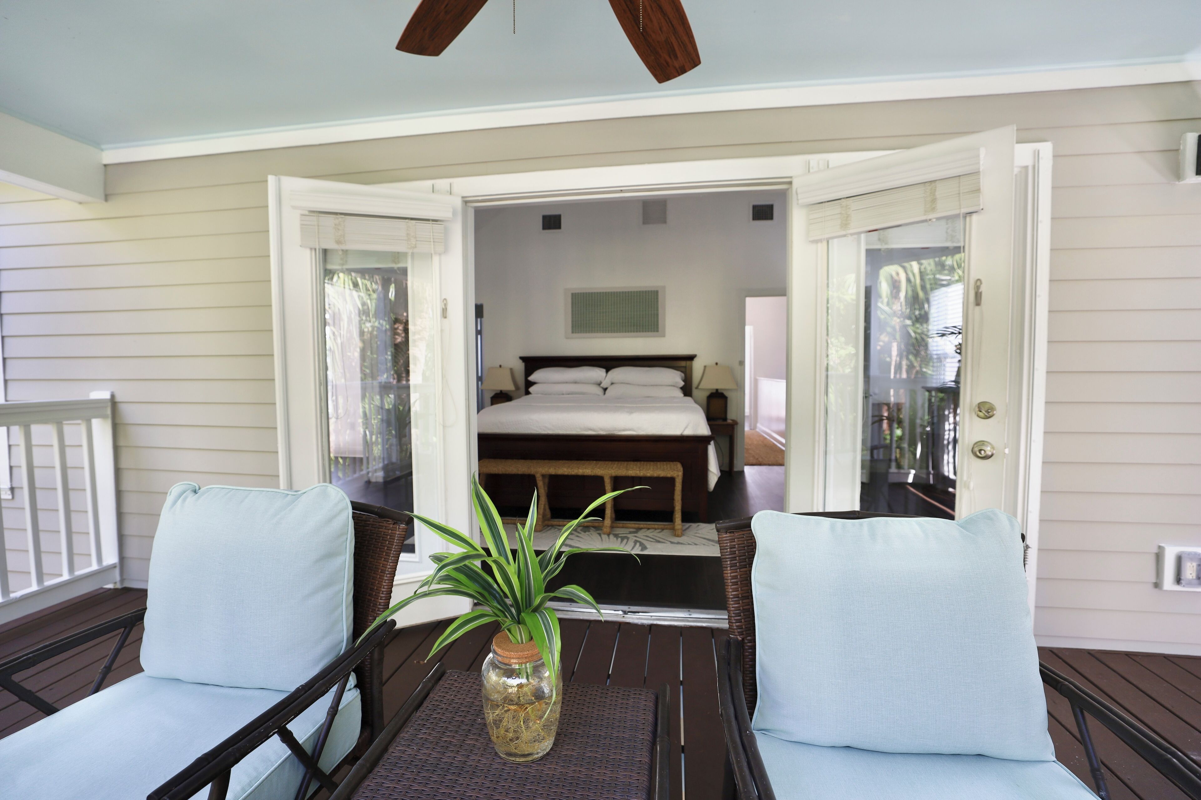 A room with a bed, a small table with a plant, and two chairs.