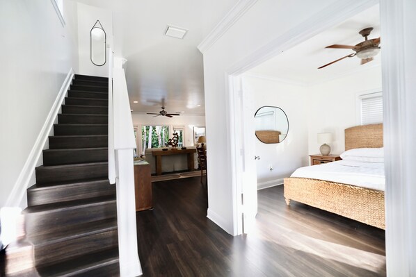 Un intérieur moderne avec un escalier en bois foncé, une chambre à coucher avec un lit en osier et un coin cuisine.