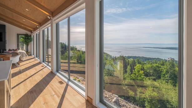 Un intérieur moderne avec de grandes fenêtres, des planchers en bois et une vue sur un lac et une forêt.