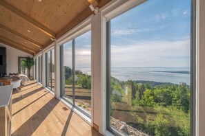 Un interior moderno con amplios ventanales, suelo de madera y vistas a un lago y un bosque.