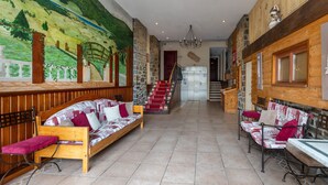 A hotel lobby with a mural, wooden benches, a staircase, and a chandelier. - Le Mont Louis - Accès direct remontées mécaniques (Les Angles)