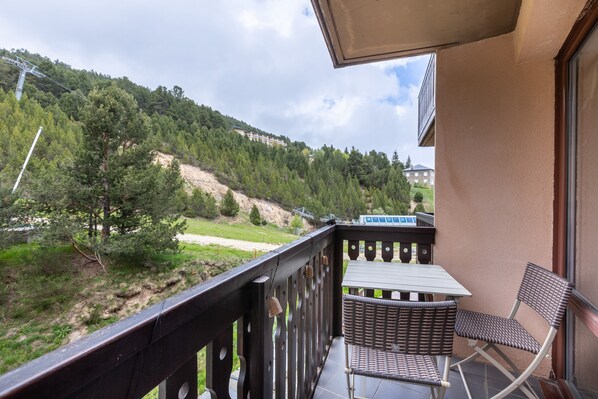 Un balcon avec des fauteuils en osier, une table et une vue sur une colline boisée.