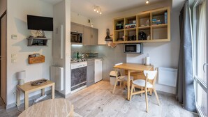 A compact kitchen with a dining area, a TV mounted on the wall, and a built-in bookshelf. - Le Mont Louis - Accès direct remontées mécaniques (Les Angles)