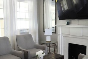 A living room with two armchairs, a small table with a vase of flowers, a flat-screen TV mounted above a fireplace, and a lamp on a side table. - River walk suite in lovely Dayton (Dayton)