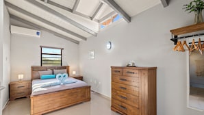 Une chambre avec un lit en bois, une commode, une fenêtre et un portant à vêtements.