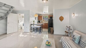 Un vaste espace de vie comprenant un coin cuisine à l’arrière-plan, une table à manger avec des chaises, un canapé et un ventilateur.