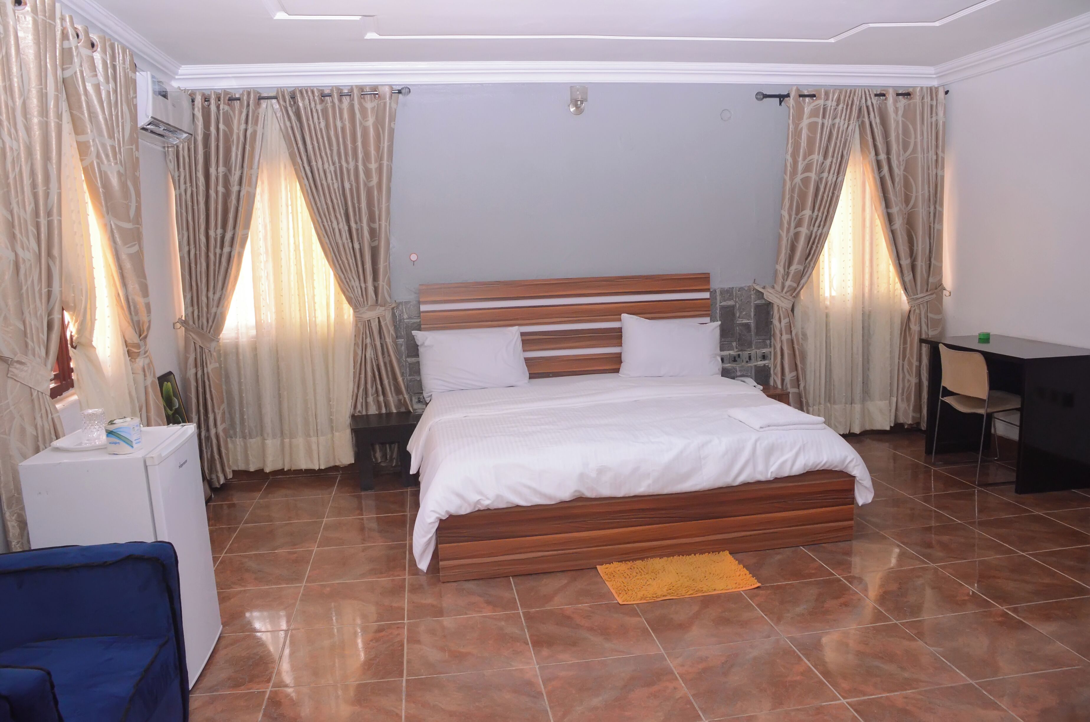 A bedroom with a wooden bed, white bedding, a desk, and a chair.