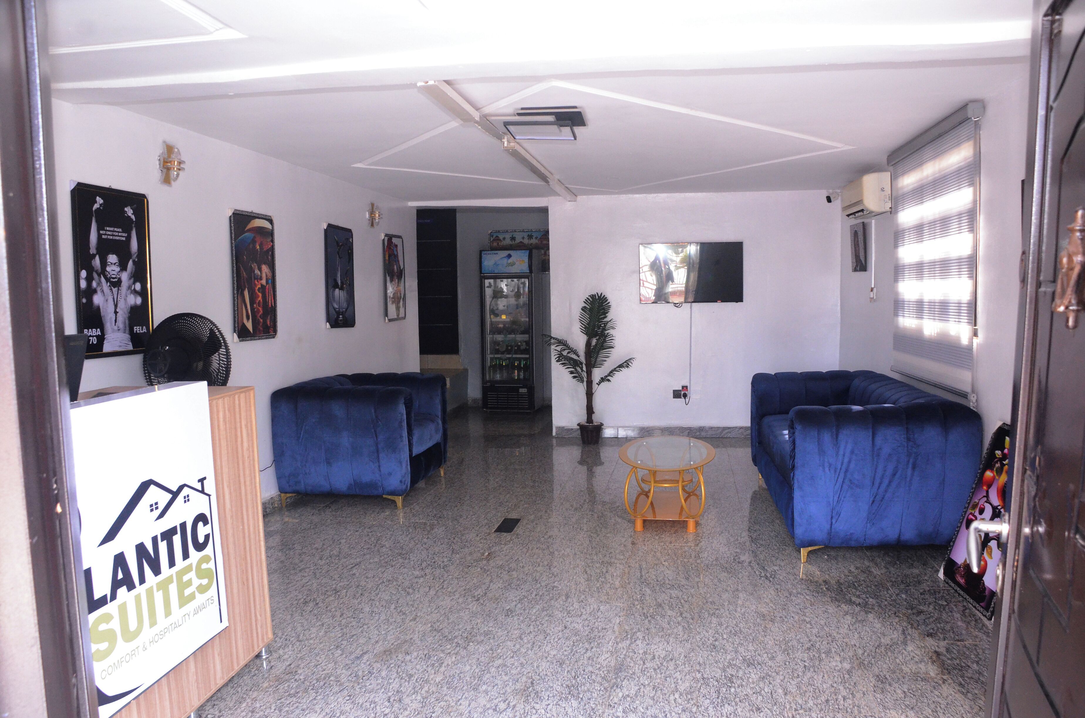A hotel lobby with two blue sofas, a small round table, a potted plant, and a refrigerator.