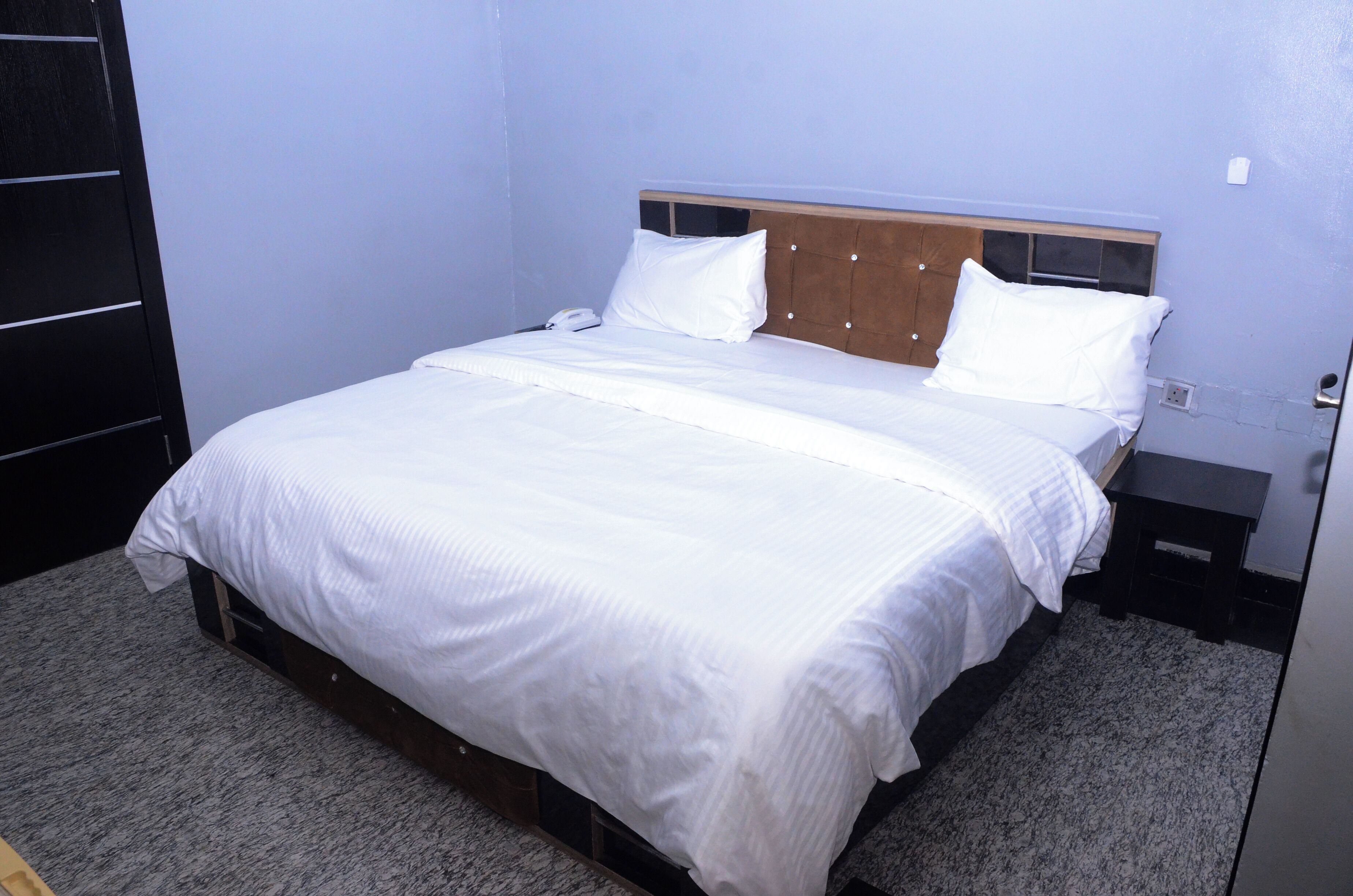 Una cama bien hecha con sábanas blancas en una habitación con paredes azul claro y un cabecero de madera.
