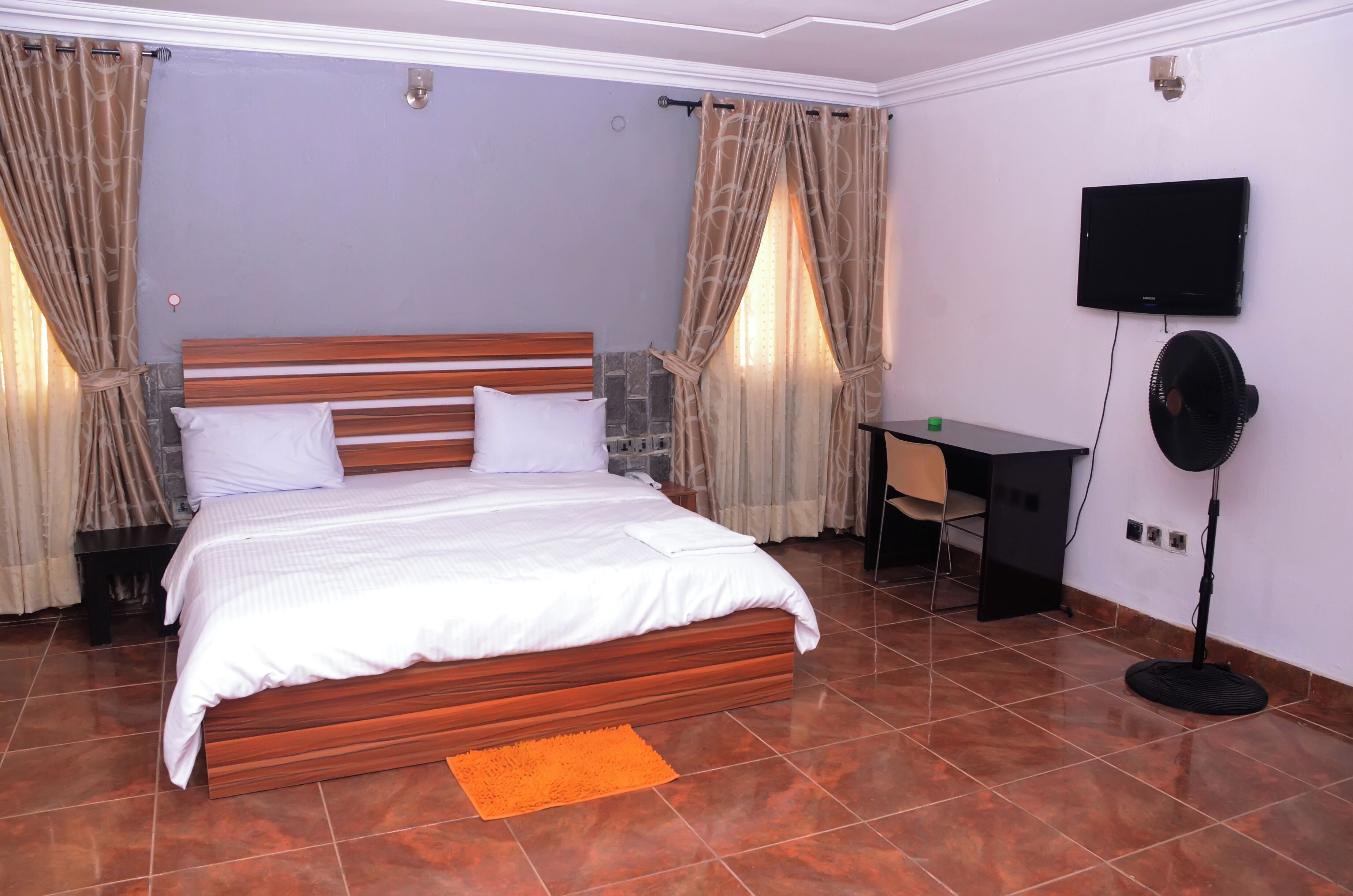 Un dormitorio con una cama de madera, un escritorio, una silla, un televisor y un ventilador de pie.