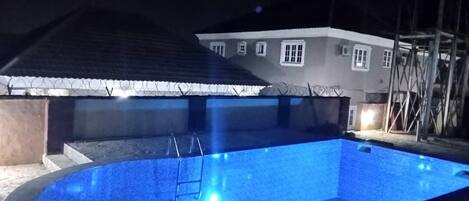 A swimming pool with a ladder, surrounded by a house with barbed wire on the roof.
