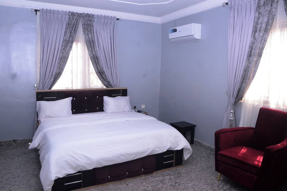 A bedroom with a bed, a red chair, and an air conditioning unit.