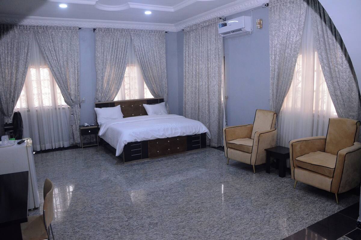 A hotel room with a bed, two armchairs, a small table, and a desk with a chair.