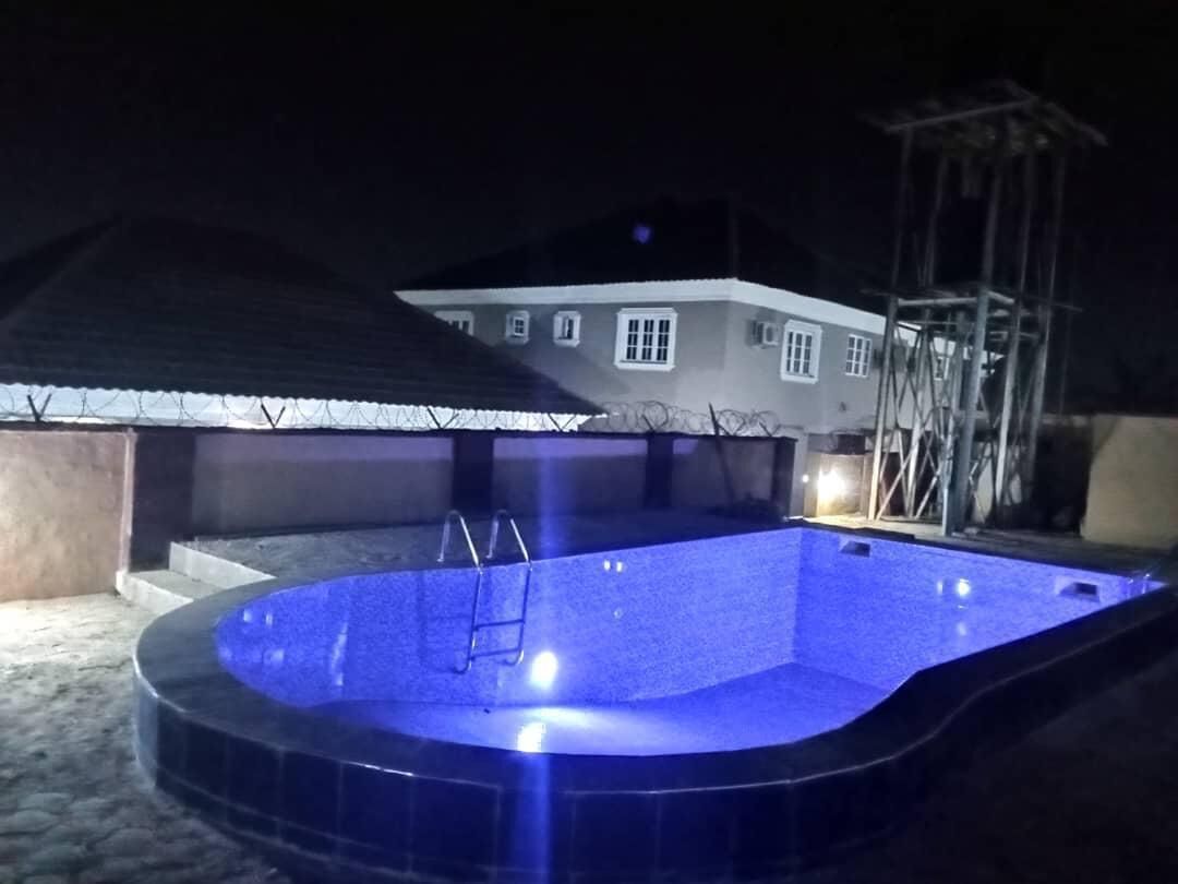 Une piscine avec un escalier, entourée d’une maison protégée par une clôture en fil de fer barbelé.